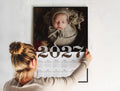 Žena věšící vytištěný kalendář 2027 na zeď – dárek pro klienty fotografa